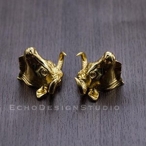 Puede incluir: Dos esculturas de cabeza de toro de oro con detalles intrincados. Las esculturas se miran y tienen un acabado ligeramente desgastado.