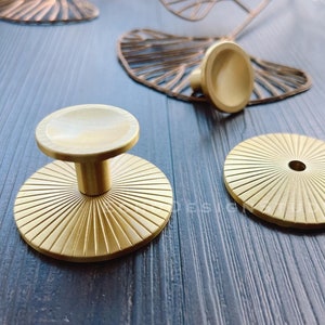 May include: Three gold metal cabinet knobs with a sunburst design. The knobs have a round base and a raised center.