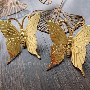 May include: Two gold metal butterfly wall decor pieces. The butterflies have detailed wings and a textured finish.