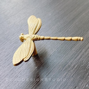 Puede incluir: Tirador de cajón de libélula dorado con alas detalladas y un cuerpo largo y segmentado.
