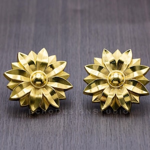 May include: A pair of gold-toned flower-shaped earrings with a textured surface.
