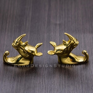May include: Two gold rhinoceros-shaped hooks facing each other. The hooks are decorative and have a shiny finish.