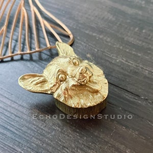 May include: A gold-colored, dog-shaped decorative object. The dog's head is detailed with fur and facial features. The object is on a dark wooden surface. The text "ECHODESIGNSTUDIO" is visible.