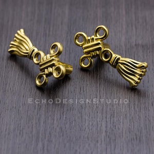May include: Two gold-coloured metal earrings with a tassel design. The earrings are in the shape of a knot with a tassel hanging from the bottom.