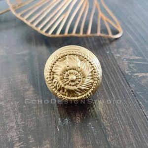 Peut inclure: Un bouton de porte rond en or avec un motif floral détaillé.