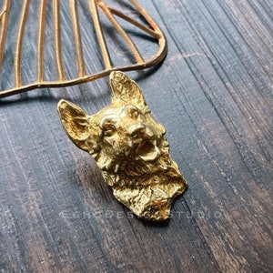 May include: A gold-coloured metal sculpture of a dog's head. The sculpture is detailed and realistic, with a textured surface. The dog's mouth is open, and its tongue is visible.