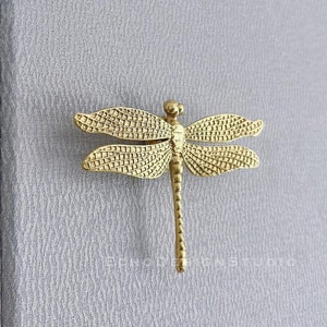 May include: Gold dragonfly drawer pull with intricate details. The pull is a decorative hardware piece for furniture.