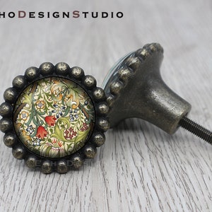 May include: Two antique brass cabinet knobs with a floral design. The knobs have a round base with a raised edge and a decorative floral pattern in the center. The knobs are attached to a metal screw.