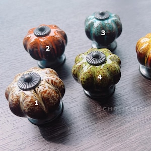 Könnte beinhalten: Fünf Keramik-Schrankknöpfe in verschiedenen Farben und Mustern. Die Knöpfe sind kürbisförmig und haben eine Metallbasis. Die Farben umfassen Orange, Gelb, Grün, Braun und Blau.