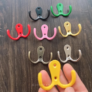 Puede incluir: Surtido de diez ganchos dobles en varios colores, incluyendo negro, rojo, rosa, verde, dorado, plateado y amarillo. Los ganchos son de metal y tienen un diseño simple y clásico.