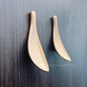 Op de afbeelding: Twee gouden, bladvormige kastgrepen, gemonteerd op een donker houten oppervlak.