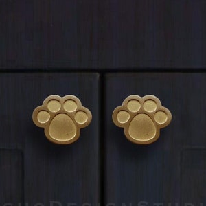 Könnte beinhalten: Zwei goldene Türknauf in Form einer Pfote an einer dunkelblauen Schranktür. Der Text "EchoDesignStudio" ist unter den Knäufen gedruckt.