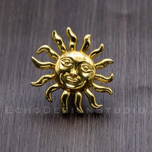 May include: A gold-colored sun with a smiling face and rays extending outward. The sun is on a dark wood background.