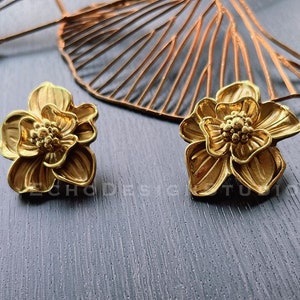 Peut inclure: Une paire de boucles d'oreilles en forme de fleur dorées. Les boucles d'oreilles sont en métal et présentent un design détaillé.
