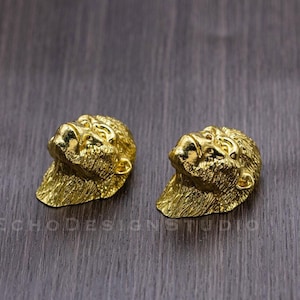 Peut inclure: Une paire de boucles d'oreilles dorées avec un design détaillé en trois dimensions d'un visage de gorille.