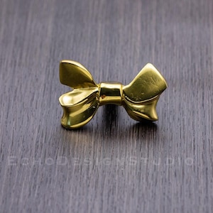 May include: A gold-colored bow-shaped cabinet knob or drawer pull.