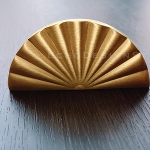 Può includere: Una maniglia per armadio in metallo color oro a forma di semicircolo con un design a raggiera.