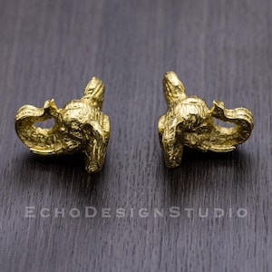 May include: Two gold-coloured elephant figurines, facing each other, on a dark wood surface.