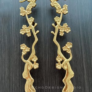 May include: A pair of gold-toned door handles featuring a floral design. The handles are shaped like a stylised tree branch with delicate flowers.