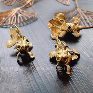 Pode incluir: Três estatuetas de peixe dourado de metal dourado. As estatuetas são detalhadas e têm uma aparência realista.