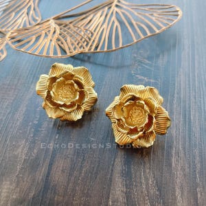 以下が含まれることがあります： 金色の花の形をしたイヤリングのペア。イヤリングは金属製で、細部までこだわったデザインです。