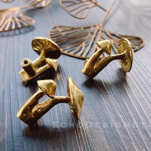 May include: Three gold-toned mushroom-shaped cabinet knobs. The knobs are made of metal and have a smooth, polished finish.