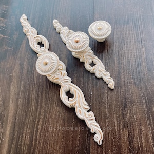 May include: Three ornate white cabinet knobs with gold accents. The knobs feature a floral design and are ideal for adding a touch of elegance to any room.