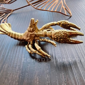 May include: A gold-colored metal lobster figurine. The lobster is posed with its claws raised and its tail curled.