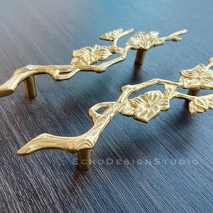 以下が含まれることがあります： スタイリッシュな枝と花のアクセントが付いた、ゴールドトーンの金属製のキャビネットドアプルが2つです。