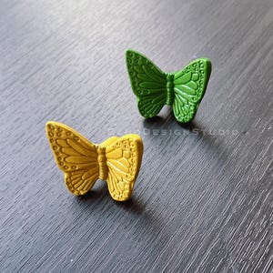 May include: Two decorative butterfly-shaped drawer pulls. One is green and the other is yellow.