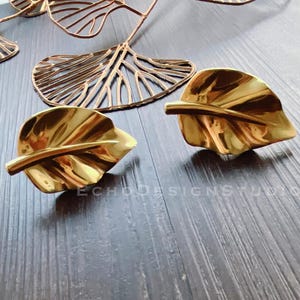 Puede incluir: Dos pendientes de hoja de oro con una superficie texturizada.