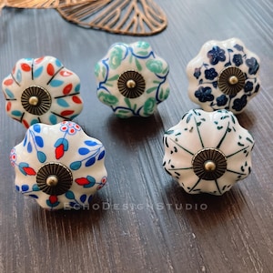 May include: Five ceramic cabinet knobs with a white base and floral patterns in blue, green, and red. Each knob has a round, gold-colored metal accent in the center.