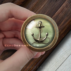 May include: A brass knob with a glass insert featuring a gold anchor and rope on a green and white background.