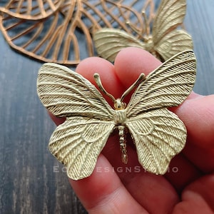 May include: A gold metal butterfly charm with a detailed textured design. The butterfly has a delicate, intricate design and is perfect for adding a touch of elegance to jewelry or crafts.