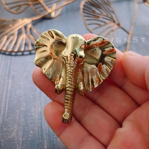 May include: A gold-colored elephant figurine with a detailed design. The figurine is made of metal and has a textured surface.