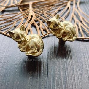 May include: Two gold-toned metal cat drawer pulls, each featuring a curled-up cat design.