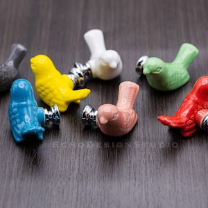 Può includere: Sette tiretti per cassetti in ceramica a forma di uccello in vari colori, tra cui blu, giallo, rosa, rosso, verde e grigio. Ogni tiretto ha una base in metallo argentato.