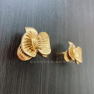 Könnte beinhalten: Ein Paar goldene Ohrstecker in Blumenform. Die Ohrringe sind aus Metall und haben ein zartes, filigranes Design.