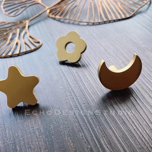 May include: Three gold-toned metal drawer pulls in the shapes of a star, a flower, and a crescent moon.