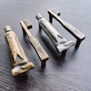 Könnte beinhalten: Vier antike Schrankknöpfe in Form von Zahnpastatuben. Die Knöpfe sind aus Metall und haben eine patinierte Oberfläche. Zwei der Knöpfe sind golden und zwei sind silbern.