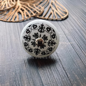 Puede incluir: Pomo de cerámica blanco con un diseño geométrico en blanco y negro. El pomo tiene un tornillo plateado en el centro.