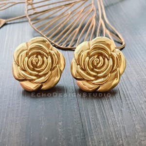 May include: A pair of gold-tone rose-shaped earrings. The earrings are made of metal and have a detailed design.