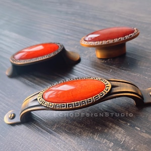 May include: Three antique-style cabinet knobs with a red stone inlay and an ornate gold-toned metal frame. The knobs are oval shaped and have a decorative border.