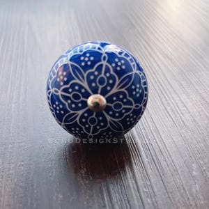 May include: A blue and white ceramic knob with a floral design. The knob has a silver metal accent in the center.