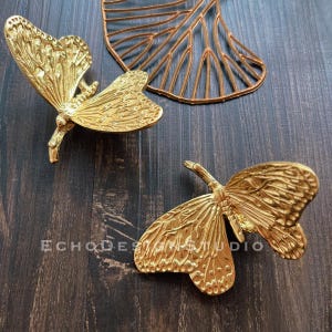 May include: Two gold-colored metal butterfly wall decor pieces. The butterflies have intricate details and a textured finish.