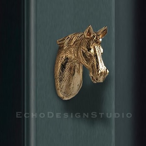 May include: Gold horse head door knob. The horse head is facing to the right. The knob is mounted on a dark blue door.