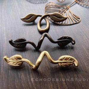 May include: Two sets of decorative cabinet pulls with a leaf design. One set is gold and the other is black.