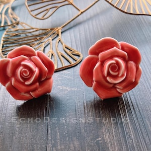 Op de afbeelding: Twee roze keramische roosvormige ladegrepen. De grepen hebben een gedetailleerd ontwerp en zijn perfect om elke woning een vleugje elegantie te geven.