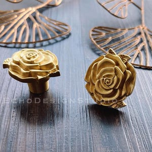 May include: Two gold-toned rose-shaped drawer pulls. The pulls have a detailed, textured design.