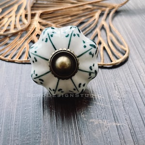 Puede incluir: Pomo de cerámica blanco con un diseño floral verde y un acento de latón. El pomo es un elemento decorativo para muebles o armarios.